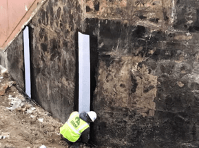 Reinforcing fabric adhered to wall with hot asphalt waterproofing